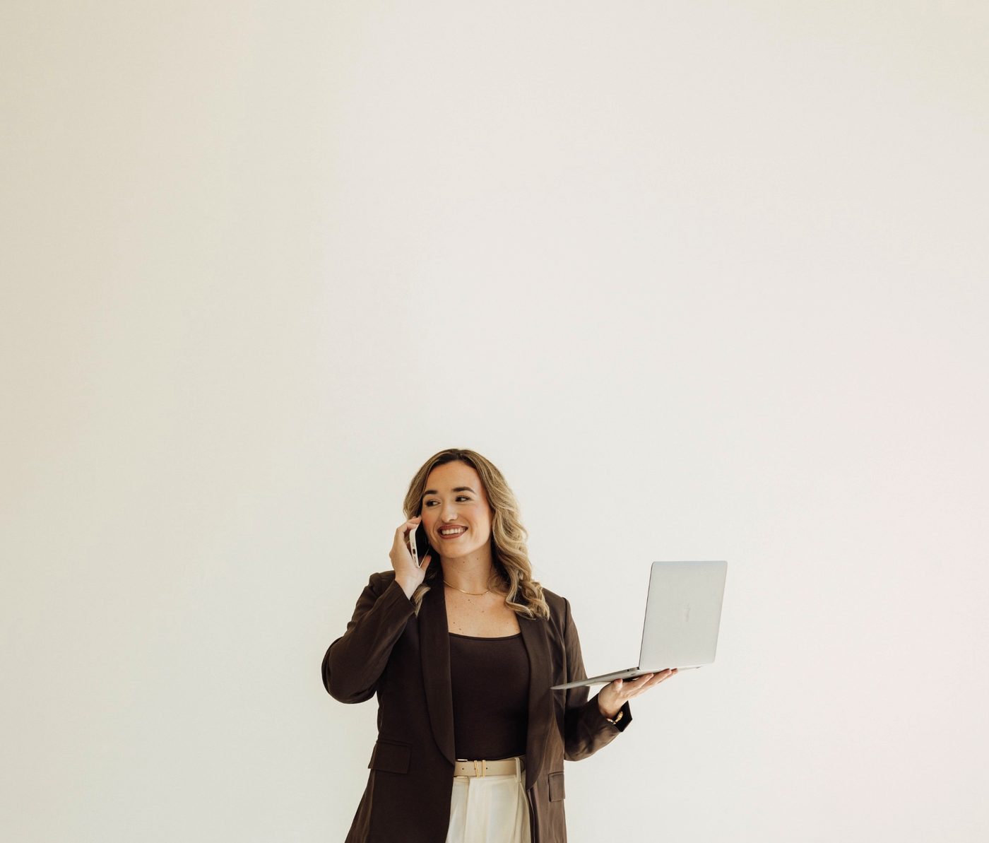 Kristin Pitts, founder of Aligned Consulting, on the phone with a laptop in hand against a plain studio wall